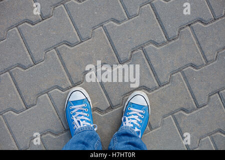 In una passeggiata - indossare scarpe da ginnastica, vista dall'alto sulla pavimentazione in calcestruzzo e scarpe blu Foto Stock