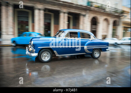 L'Avana, Cuba - 18 Maggio 2011: classica degli anni cinquanta unità auto in motion blur attraverso le strade bagnate di Centro dopo un acquazzone. Foto Stock