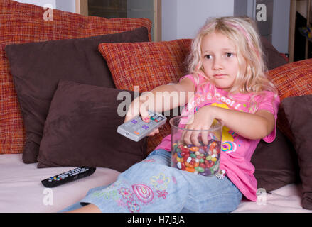 Ragazza con i dolci e il controllo in remoto di guardare la TV Foto Stock