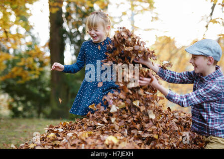 Felice l'autunno. Due bambini che giocavano in foglie secche palo in autunno park. Foto Stock