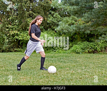 Ragazza giovane sull'erba calci ad un pallone da calcio e sorridente Foto Stock