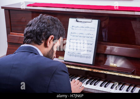 L'uomo suonare il pianoforte mentre è seduto, leggendo gli appunti e guardando verso il basso Foto Stock