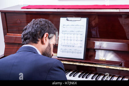 L'uomo suonare il pianoforte pianoforte canzone da note durante la seduta, guardando verso il basso Foto Stock
