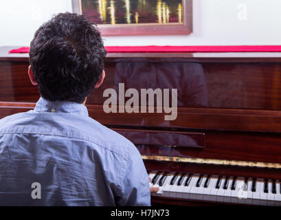 L'uomo suonare il pianoforte mentre è seduto e guardando indossando maglietta blu capelli irregolare Foto Stock