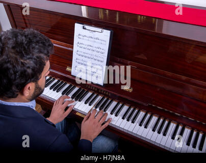 L'uomo suonare il piano utilizzando note durante la seduta, ragazzo suonare il pianoforte con seduta e panno rosso sul pianoforte Foto Stock