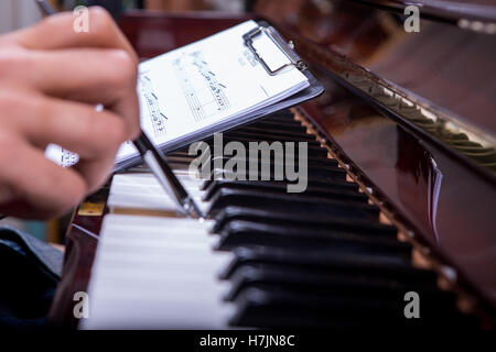 L'uomo suonare il pianoforte con penna a sfera e tenendo note nella mano sinistra Foto Stock