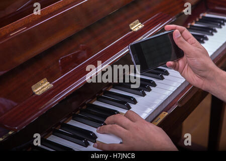 L'uomo suonando piano tenendo il telefono in mano destra Foto Stock