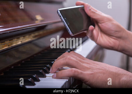 L'uomo suonare il pianoforte dal telefono cellulare, tenendo il telefono mobile nella mano destra e giocare con la mano sinistra Foto Stock