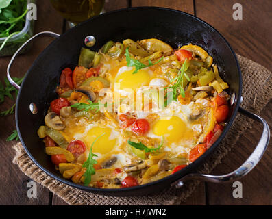 Uova fritte con le verdure in una padella su un sfondo di legno. Foto Stock