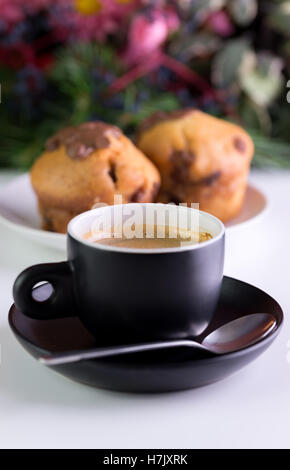 Caffè del mattino in tazza nera con muffin dietro. Foto Stock