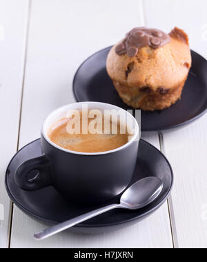 Caffè del mattino in tazza nera con muffin dietro. Foto Stock