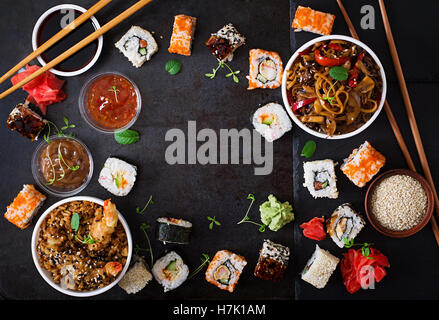 Tradizionale cibo giapponese - sushi, rotoli, Riso con gamberi e udon tagliatelle con pollo e funghi su uno sfondo scuro. Parte superiore Foto Stock