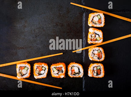 Tradizionale cibo giapponese - sushi, rotoli e bacchette per sushi su uno sfondo scuro. Vista superiore Foto Stock