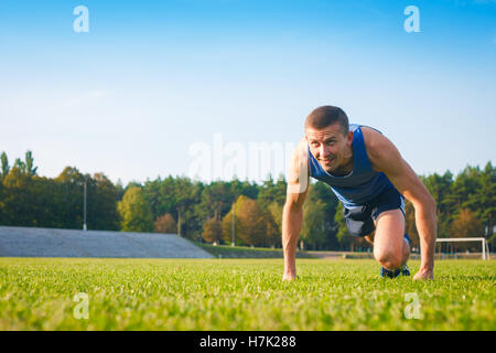 Uomo in bassa posizione di avviamento sul vecchio stadio. Atleta in posizione di partenza. In esecuzione, jogging, cardio, sport, stile di vita attivo concep Foto Stock