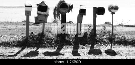 Sei Caselle lettera per diversi indirizzi in un paese di campagna. Essi stanno gettando ombre sul terreno con un lago rurale sullo sfondo. Foto Stock