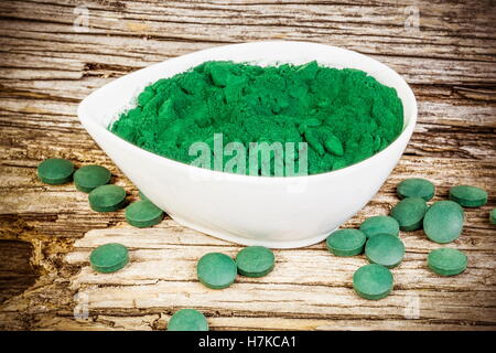 Spirulina,chlorella supplemento polvere e pillole in bianco ciotola e su legno Foto Stock
