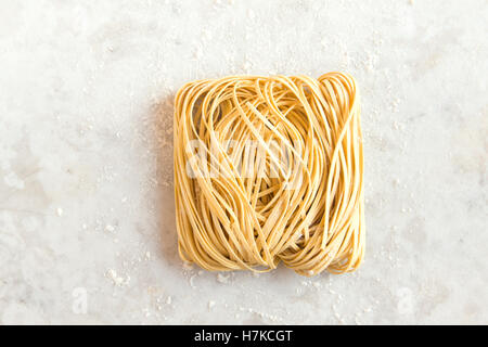 Materie non cotti in casa la pasta italiana Le tagliatelle (cinese di noodle all'uovo) oltre rustico in pietra bianca con uno sfondo con spazio di copia Foto Stock