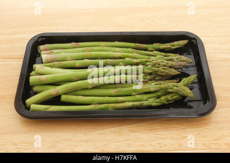 I germogli di asparagi in un vassoio di plastica su un tagliere di legno Foto Stock