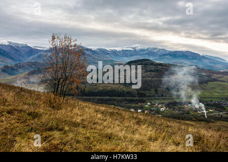 Montagne alte vette innevate su area rurale in autunno sotto il cielo nuvoloso Foto Stock