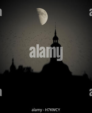 Stormo di uccelli in volo edificio passato la notte con mezza luna in background. Dark, moody e spooky impostazione con la fauna selvatica a t Foto Stock