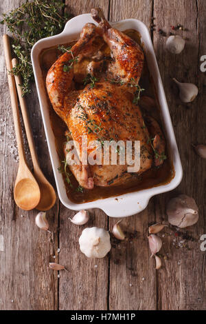 Cibo francese: pollo con quaranta spicchi di aglio nel piatto di cottura e ingredienti di close-up sul tavolo. vista verticale fro Foto Stock