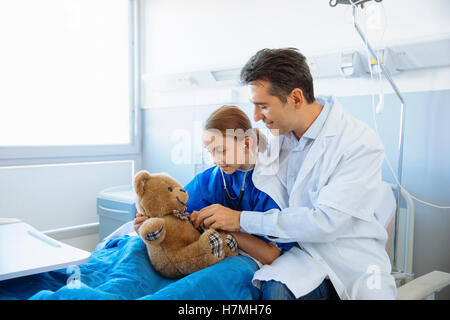 Medico e paziente ragazza esaminando un orsacchiotto Foto Stock