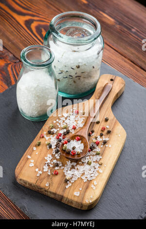 Sale in vasi di vetro e cosparsi con sale e pepe, oliva cucchiaio di legno sul bordo di taglio Foto Stock