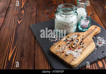 Sale in vasi di vetro e cosparsi con sale e pepe, oliva cucchiaio di legno sul bordo di taglio Foto Stock