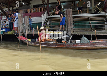 Un cibo galleggiante fornitore cucina nella sua canoa in un canale il Mercato Galleggiante di Damnoen Saduak, vicino a Bangkok, in Thailandia Foto Stock