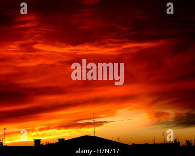 Arrabbiato di rosso le nuvole in bilico sopra le case al tramonto. Ripresa a tutto campo del cielo di sera in Italia. Foto Stock