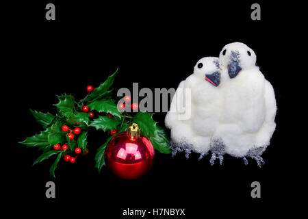 Due figure di pinguino insieme con baubles e holly bacche isolati su sfondo nero Foto Stock