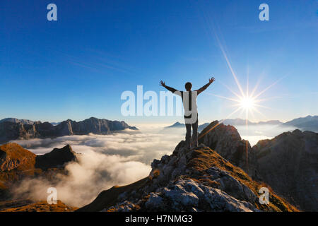 Scalatore sulla sommità del picco di montagna con mani spred watchiing sun Foto Stock