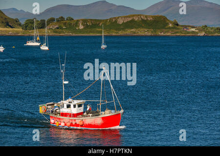 Isola Kerrera vista con le navi a vela. Rosso barca dei pescatori di fronte. Foto Stock