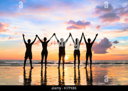 Silhouette di un gruppo di persone che si tengono per mano fino in spiaggia con un bel tramonto - concetto circa il lavoro di squadra, amicizia Foto Stock