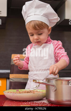 Poco carino bambino mette lo zucchero in una terrina in cucina. Madre di helper. 2 anno di età. Foto Stock