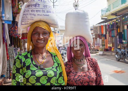 Due donne che portano i sacchi di riso o di farina sulle loro teste nel tradizionale modo indiano, Pushkar, India Foto Stock