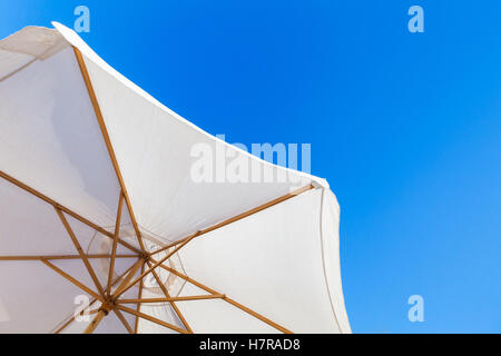 Bianco ombrello aperto sotto il luminoso cielo blu in giornata estiva, resort foto di sfondo Foto Stock