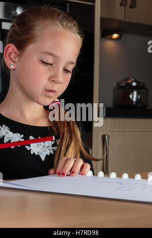 Ragazza giovane pensare mentre si fanno i compiti al tavolo della cucina tenendo premuto matita Foto Stock