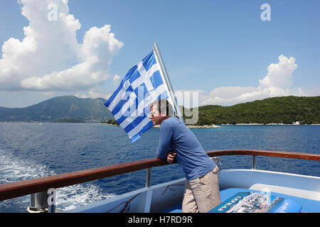 Nidri, Grecia, 11 Maggio 2013: l'uomo e la bandiera greca sulla barca in mare Ionio. La Grecia. Foto Stock