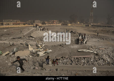 Qayyarah, Niniveh, Iraq. 8 Novembre, 2016. 08/11/2016. Qayyarah, Iraq. Il fumo proveniente da olio in fiamme facilties riempie il cielo come uomini pila di blocchi in calcestruzzo e giovane iracheno ragazzi giocano tra distrutto football Stadium di Qayyarah, Iraq. Lo stadio è stata bersaglio di un iracheno o coalizione airstrike come era la posizione per una sede di ISIS. Pozzi di petrolio in e intorno alla città di Qayyarah, Iraq, abbiamo impostato acceso nel Luglio 2016 da uno Stato islamico gli estremisti come l esercito iracheno ha iniziato un offensiva per liberato la città. Credito: ZUMA Press, Inc./Alamy Live News Foto Stock