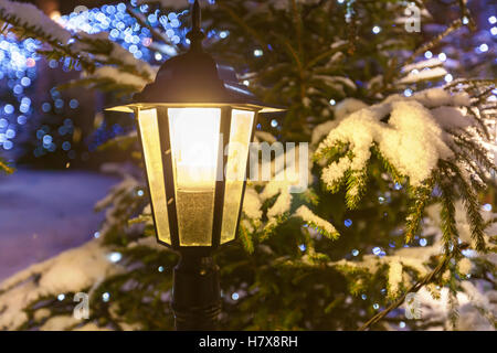 Lampione. Switched-sulla strada lampada contro l albero di Natale decorato e ghirlande nella neve vicino. Foto Stock