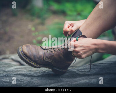 Una giovane donna è seduta su un registro nella foresta e legatura è il suo stivali Foto Stock