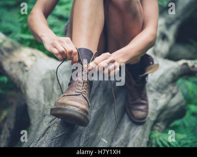 Una giovane donna è seduta su un registro nella foresta e legatura è il suo stivali Foto Stock