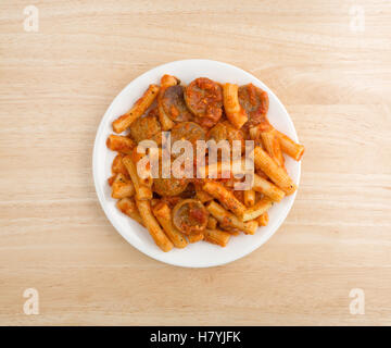 In alto di un serving di rigatoni pasta con salsiccia e polpette di carne in salsa marinara su una piastra in cima a una tavola di legno. Foto Stock