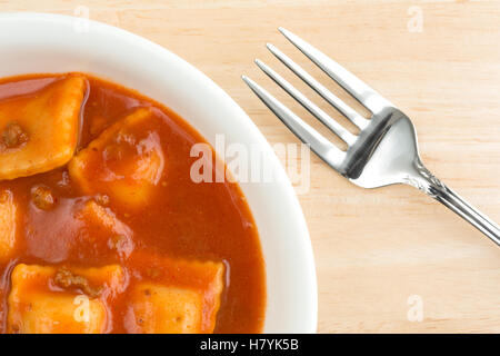 Top vista ravvicinata di un serving di ravioli in una ciotola su una tavola di legno con una forcella a lato. Foto Stock