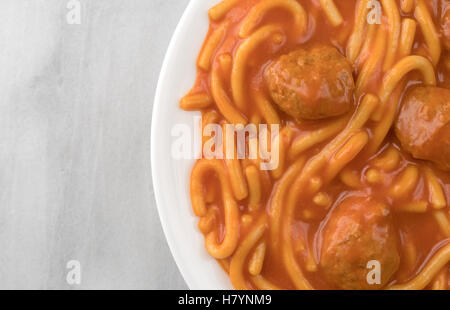 Top vista ravvicinata di una porzione di spaghetti e polpette di carne su una piastra bianca sulla cima di un marmo grigio tavolo. Foto Stock