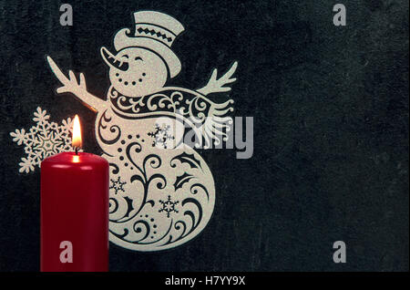 White Label pupazzo di neve,il simbolo del fiocco di neve e la masterizzazione di rosso candela su una pietra scura sullo sfondo. Decorazione di natale con copia spazio. Chiudere, ho Foto Stock