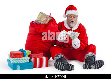 Babbo Natale seduto accanto al dono di contare una nota di valuta Foto Stock