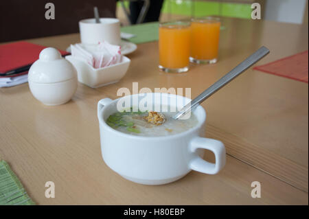 Pollo salutare una zuppa di riso in una tazza bianca con un cucchiaio collocato su un tavolo di legno con sfondo sfocato. Foto Stock