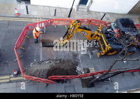 JCB digger scava per lavori stradali in London side Street, Londra Foto Stock